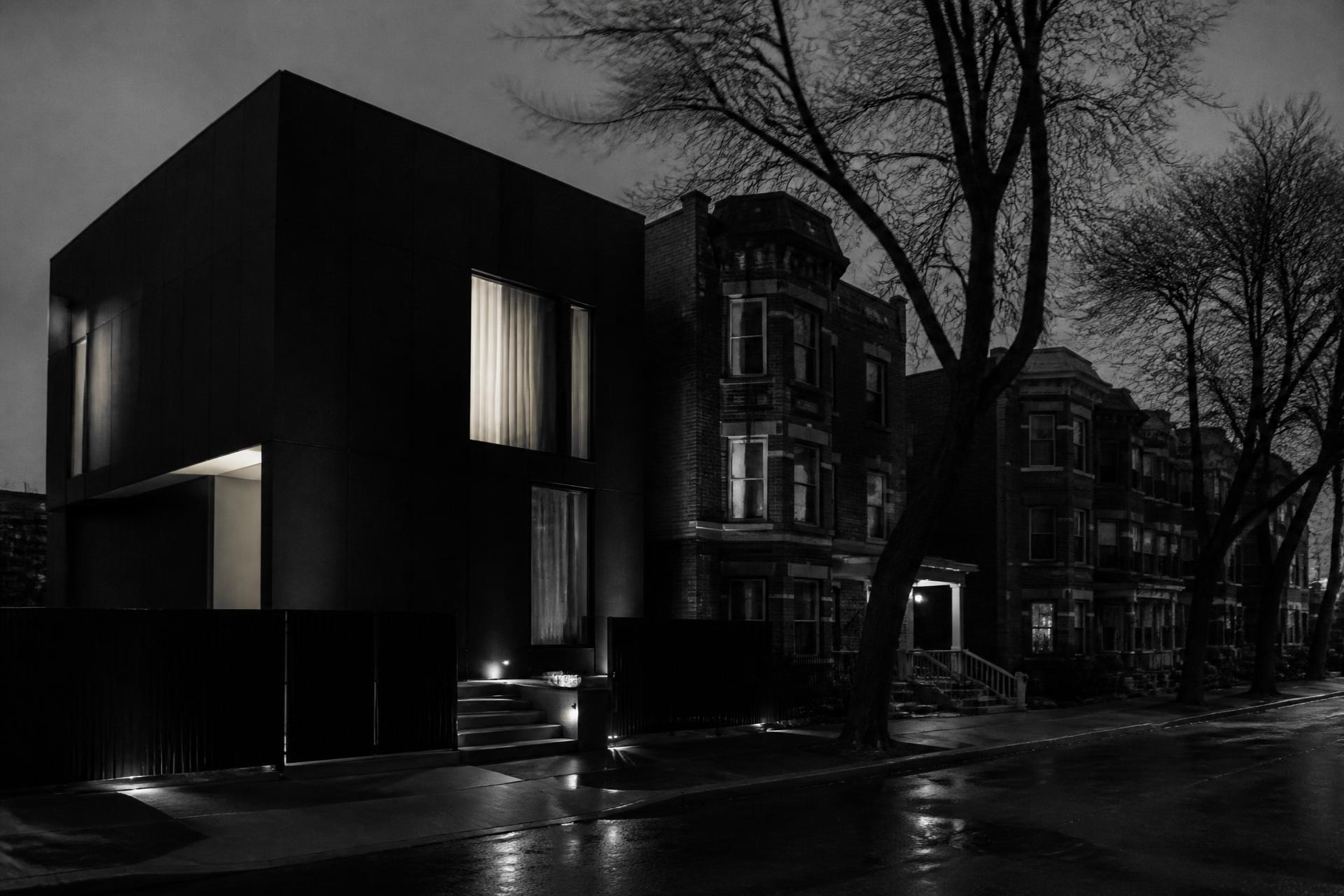 A modern black house standing on the left side of a Chicago residential block at night